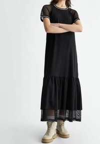 Czarna sukienka z krótkimi siateczkowymi rękawami, okrągłym dekoltem i falbaniastym wykończeniem u dołu. Noszona z beżowymi botkami na sznurówki.