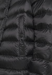 Sort pufferjakke med quiltede sektioner, glat tekstur og knapdetalje på forsiden.