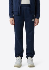 Navy blue fleece joggers with an elastic waistband, featuring The North Face logo in white on the left thigh and cuffed ankles.