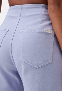 Lichtblauwe high-waisted broek met een gestructureerde afwerking, voorzien van twee achterzakken en een klein label op de rechterzak.