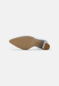 Zapato de tacón alto en azul claro con punta afilada, textura de gamuza suave y suela de goma con patrones estriados para mayor tracción.
