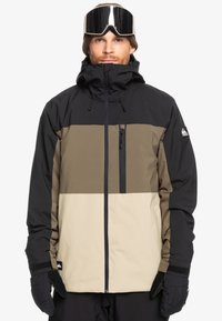 Veste d'extérieur pour hommes avec un design coloré en blocs de noir, marron et beige, dotée d'un col haut, d'une poche zippée et de poignets réglables.
