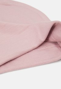 Tecido de algodão rosa claro com uma textura suave, apresentando uma borda dobrada. A costura está acabada de forma cuidada, mostrando um design simples.