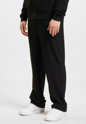 Svart joggebukser med en avslappet passform, laget av mykt stoff, med sidelommer og elastiske mansjetter. Sammen med hvite joggesko.