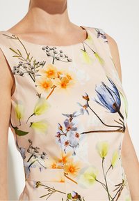 Robe à fleurs en tissu rose clair ornée de fleurs jaunes, bleues et blanches vives. Texture lisse, sans manches, avec un décolleté bateau.