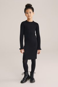 Svart ringad klänning med långa ärmar, volangmanchetter, åtsittande siluett, bärs med svarta strumpbyxor och lackläderkängor.