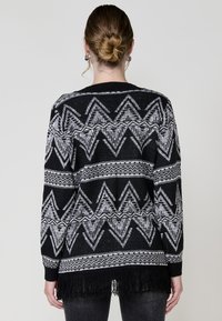 Maglione lavorato a maglia in bianco e nero con un motivo a zigzag, dotato di maniche lunghe, orlo frangiato e scollatura a coste.