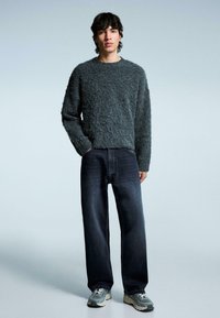 Grau melierter Pullover mit Rundhalsausschnitt, kombiniert mit dunkelblauen Jeans mit geradem Bein und grauen Sneakers. Einfaches Design und strukturierter Stoff.