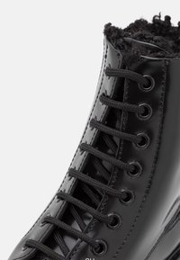 Sort patentlæderstøvle med sorte snørebånd, med en blød, pjusket foring ved kraven og øjer til snørebånd.