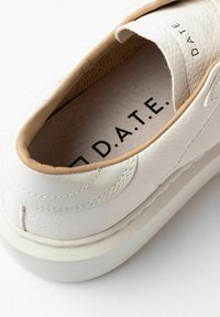 Tæt på et hvidt lædersneaker med beige trim og sort "D.A.T.E." logo synligt indeni og på tungen.