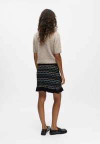 Pull court en tricot beige à manches courtes associé à une jupe noire ornée de motifs géométriques bleus et blancs complexes et d'un ourlet festonné. Chaussures plates noires.