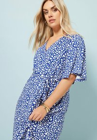 Sininen ja valkoinen kuvioitu mekko, joka on kietaisumallinen, lyhyet lepattelevat hihat ja solmittu vyötärö. Sujuva kangas, jossa on teksturoitu kuvio.