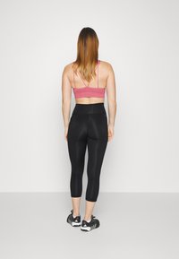 Pink sports bra with thin straps paired with black, high-waisted capri leggings. Black athletic shoes complete the outfit.