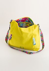Bolso amarillo con un exterior texturizado. Tiene un forro interior colorido y con estampados, y una correa ajustable también estampada. Incluye un pequeño bolsillo exterior.