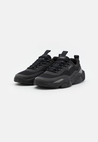 Scarpe atletiche nere realizzate in mesh e materiali sintetici, caratterizzate da una suola spessa e testurizzata e un design con lacci con un marchio distintivo.