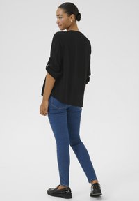 Haut noir à manches longues avec manches retroussées, associé à un jean bleu slim et des chaussures noires brillantes. Design simple, texture lisse.