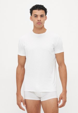 White short-sleeve t-shirt featuring subtle textured branding, round neckline, and slim fit. Paired with white briefs.