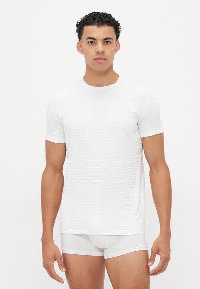 White short-sleeve t-shirt featuring subtle textured branding, round neckline, and slim fit. Paired with white briefs.