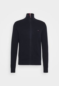 Suéter navy con cremallera y cuello alto, de tela texturizada y puños acanalados. Presenta un pequeño logotipo en el pecho y un cuello interior en contraste.