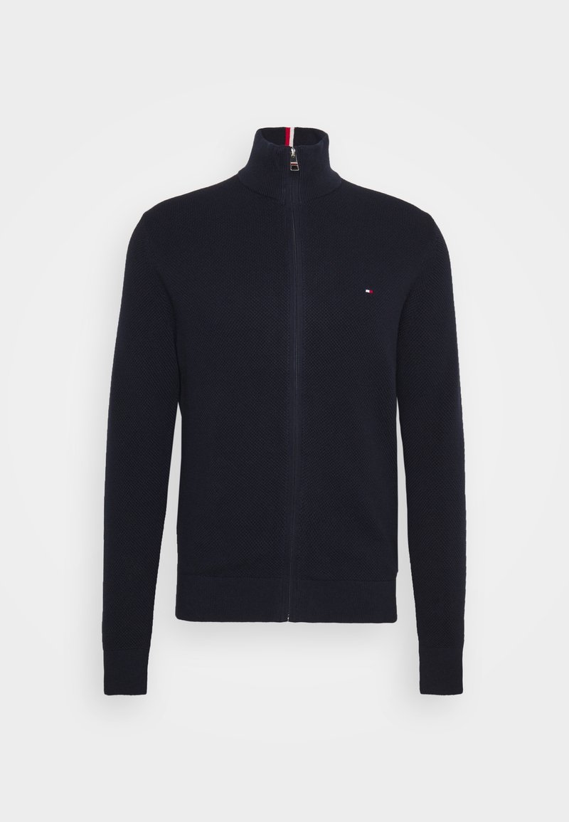 Suéter navy con cremallera y cuello alto, de tela texturizada y puños acanalados. Presenta un pequeño logotipo en el pecho y un cuello interior en contraste.