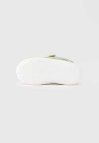 Πράσινο αθλητικό παπούτσι με υφασμάτινο αεριζόμενο επάνω μέρος με υφή, ρυθμιζόμενο λουράκι, και λευκή ελαστική σόλα με σχέδιο κυψελών.