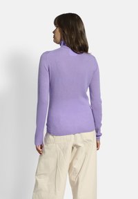 Lilafarbener Pullover mit langen Ärmeln und Rollkragen aus weichem Stoff, mit enganliegendem Schnitt und geripptem Muster, kombiniert mit off-white, locker sitzenden Hosen.