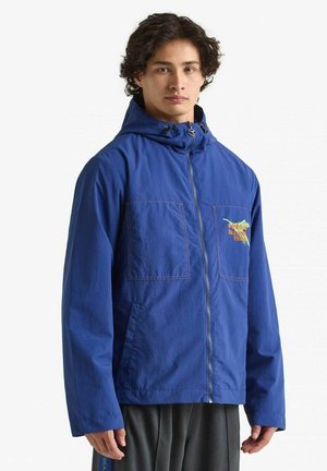 Blauwe nylon jas met een capuchon, voorzien van twee borstzakken, geborduurde accenten en een ritssluiting. Geverfde stof met een casual pasvorm.