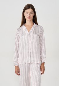 Pajama w paski w miękkim, jasnoróżowym materiale. Longsleeve z zapięciem na guziki i kieszenią. Dopasowane spodnie o luźnym kroju.