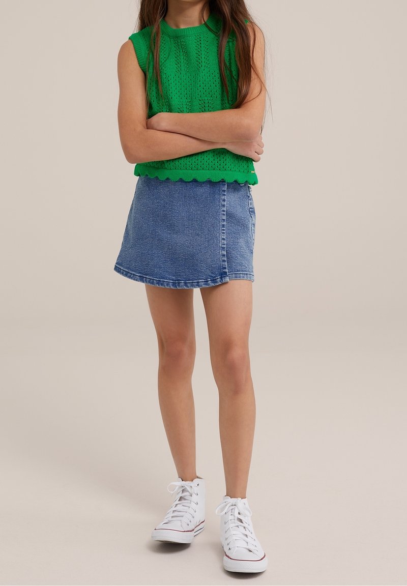 Haut vert tricoté à manches courtes avec ourlet festonné, associé à une jupe trapèze en denim bleu et des baskets montantes blanches. Design simple et épuré.