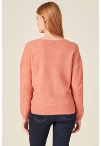 Helles korallenfarbige Strickpullover mit lockerer Passform, weitem Bootsausschnitt und gerippten Bündchen. Weiche Textur, minimale Nähte und gemütliches Design.