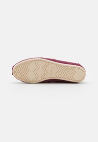 Burgundy canvas slip-on shoe with a textured light beige rubber outsole featuring zigzag and diamond patterns. TOMS logo on the outsole.