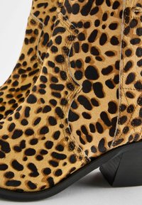 Kotníkové boty s leopardím vzorem vyrobené z texturovaných hnědých a černých chlupů, s nízkým stohovaným podpatkem a vyztuženým prošíváním na bocích.