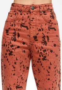 Rudos spalvos džinsai turi dėmėtą juodą raštą, penkias kišenes ir metalinį mygtuko užsegimą. Medžiaga yra minkšta ir tvirta.