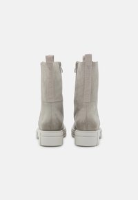 Bottes basses en cuir beige à texture lisse, avec une fermeture éclair arrière et des panneaux latéraux élastiques, et une semelle épaisse en caoutchouc blanc.