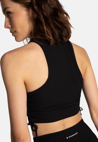 Zwarte geribbelde sport crop top met verstelbare zijbanden, hoge halslijn en open rug voor verbeterde ademend vermogen en comfort.