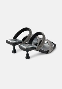 Sandali neri con tacco alto caratterizzati da due cinghie incrociate con dettagli metallici, punta quadrata e un design del tacco unico a forma di triangolo.