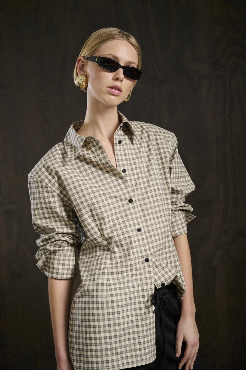 Camicia button-up a quadri beige e marrone con maniche lunghe, vestibilità morbida e colletto leggermente aperto. Indossata con pantaloni neri e occhiali da sole.