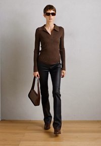 Rjava rebrasta dolgosleeve majica s ovratnikom in subtilnimi okraski, v kombinaciji s črnimi razširjenimi hlačami in rjavimi čevlji s peto. Rjava torba in sončna očala.