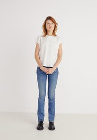 Camiseta blanca de manga corta con cuello redondo, combinada con jeans ajustados azules y zapatos negros. Diseño simple, sin patrones notables.