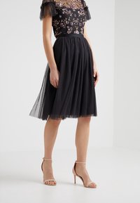 Sort tylskørt med polkaprikket tekstur, med en blomstermotiveret bodice og gennemsigtige ærmer. Kombineret med nude, snørebåndsål højhæle.