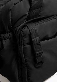 Zaino nero imbottito con tessuto testurizzato, dotato di una chiusura con zip laterale e un resistente dettaglio della tracolla per fissare gli oggetti.