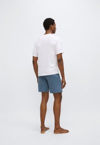 White short-sleeve shirt paired with textured blue shorts. The shirt features a round neckline; shorts have a checkered pattern.