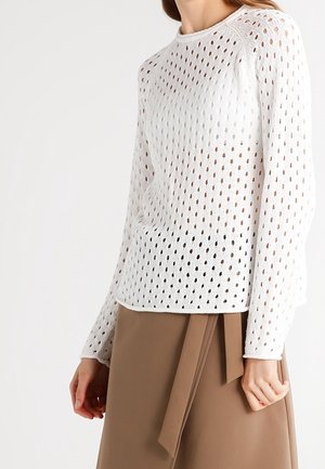 Maglione bianco a maniche lunghe lavorato a maglia con una trama aperta a motivo e scollatura rotonda, abbinato a una gonna marrone a vita alta con un nodo frontale.