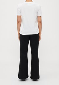 Camiseta blanca de manga corta con cuello redondo, combinada con pantalones negros acampanados. El conjunto es minimalista con una textura suave.