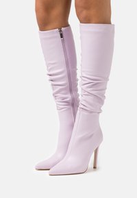 Bottes hauteur genou lilas en matière synthétique lisse, avec un bout pointu, un talon stiletto haut et une fermeture éclair latérale avec un effet froncé.