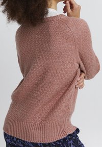 Pull rose poussiéreux texturé avec un ourlet côtelé, un col rond et des manches larges, présenté de profil.