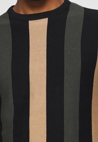 Pull en tricot présentant des rayures verticales noir, vert foncé et marron clair. Col rond avec une texture lisse.