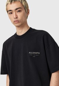 Zwarte katoenen t-shirt met korte mouwen, een ronde hals en het "ALLSAINTS" logo in zilver geborduurd op de linkerborst.