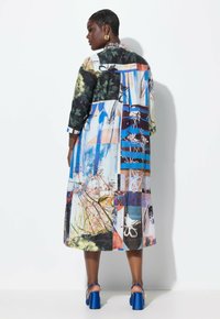 Pitkä mekko, jossa on läpatchwork-kuviointi, jossa esiintyy kukka- ja abstrakteja printtejä sinisen, vihreän ja mustan sävyissä. Valmistettu kevyestä kankaasta, jossa on 3/4-hihoja.