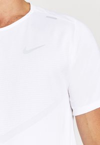 Biała koszulka sportowa z okrągłym dekoltem, krótkimi rękawami, teksturowanym wzorem i jasnoszarym logo Nike na klatce piersiowej.